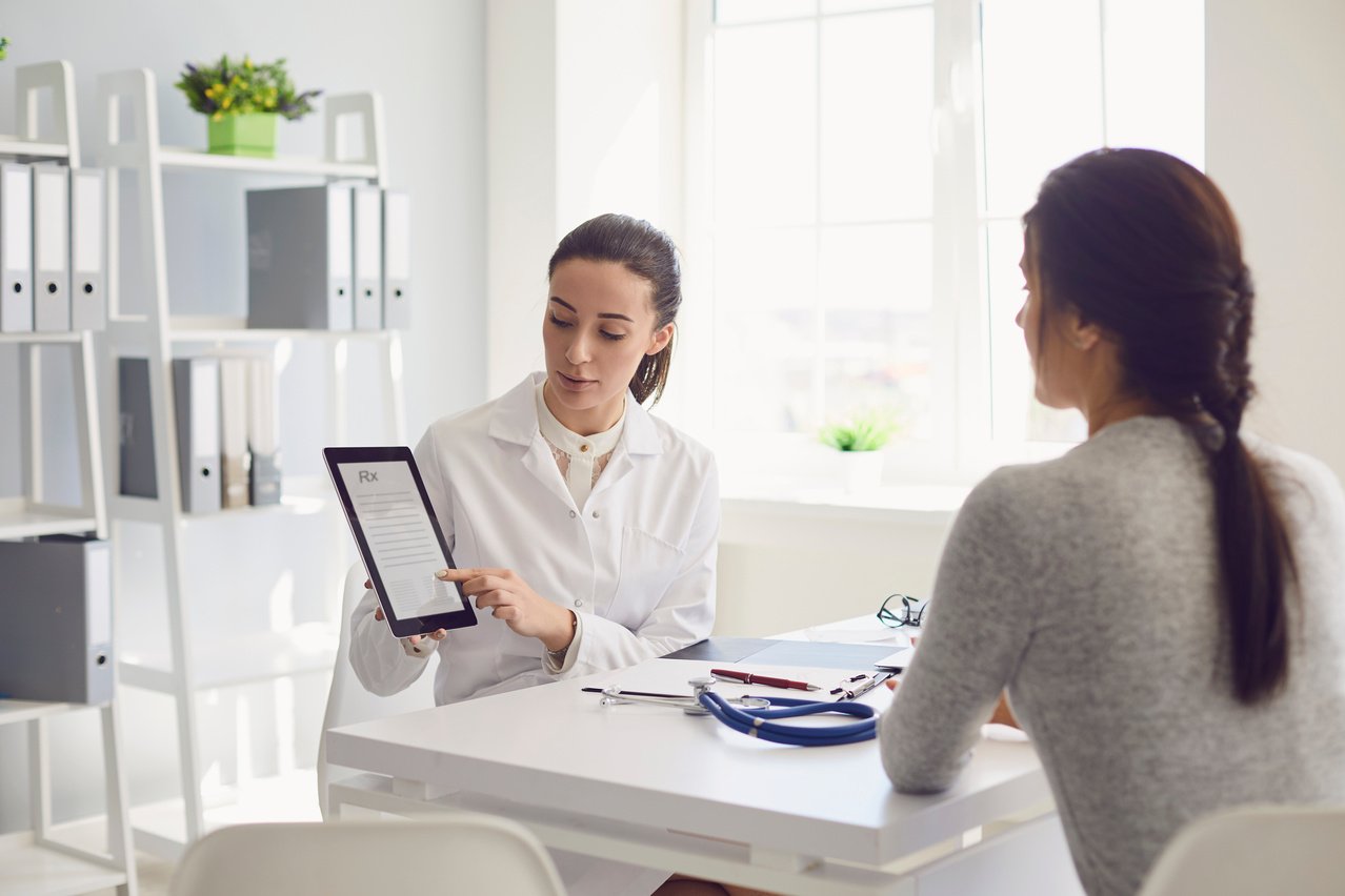 Woman Patient Visiting Female Doctor at Clinic Office. Medical Work Writes a Prescription on a Table in a Hospital.