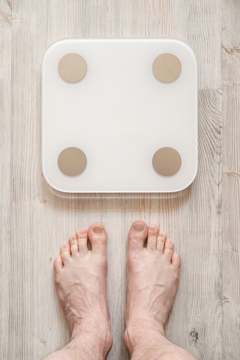 Male bare feet stand next to smart scales that makes bioelectric impedance analysis, BIA, body fat measurement. Top view.